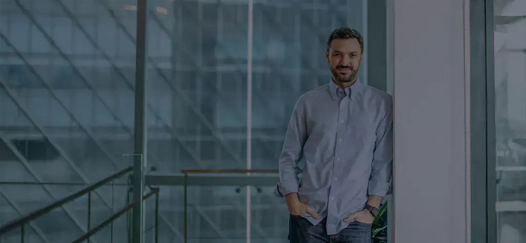 Professional standing in a modern office with glass walls and urban skyline in the background.