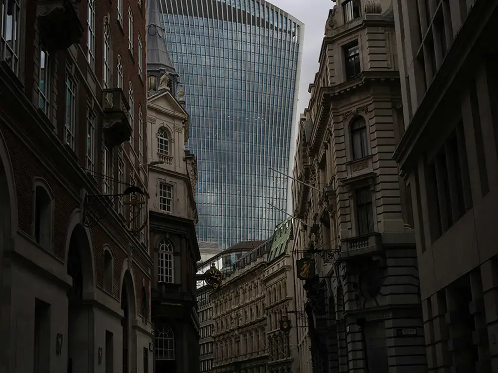 Modern glass skyscraper rises behind historic buildings on a narrow city street in London.