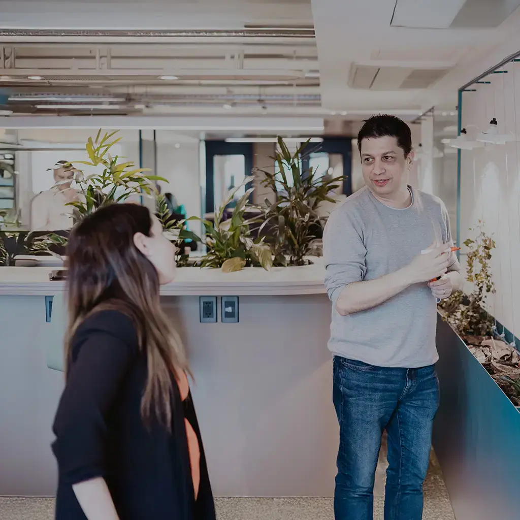 Colleagues in a modern office discuss ideas while one writes on a glass whiteboard.