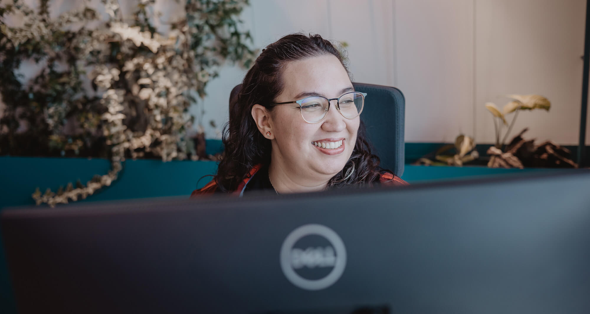Smiling team member working at a desk with a large monitor in a modern office setting.