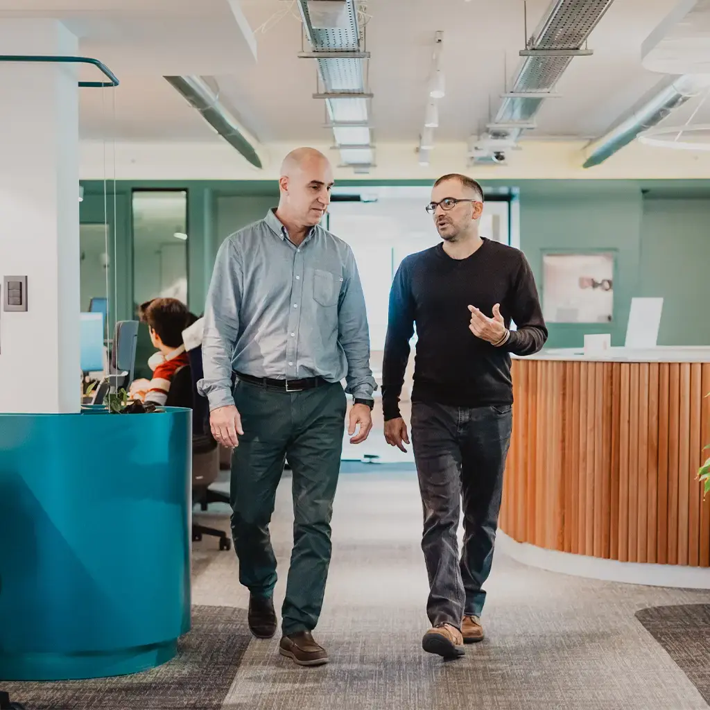 Two colleagues walking and discussing in a modern, open-plan office environment.