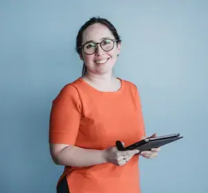 A professional smiling and holding a tablet against a plain blue background.