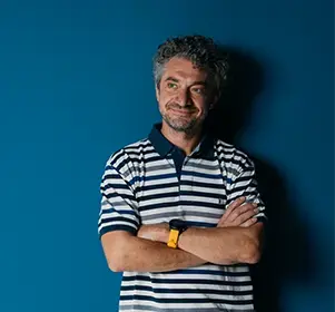A professional standing confidently with arms crossed, smiling against a solid blue background