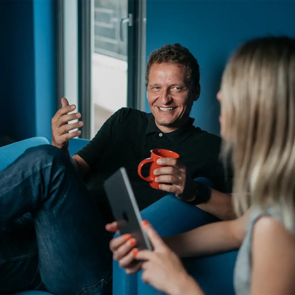 Colleagues in discussion during a casual office meeting, with tablet and coffee in a modern workspace