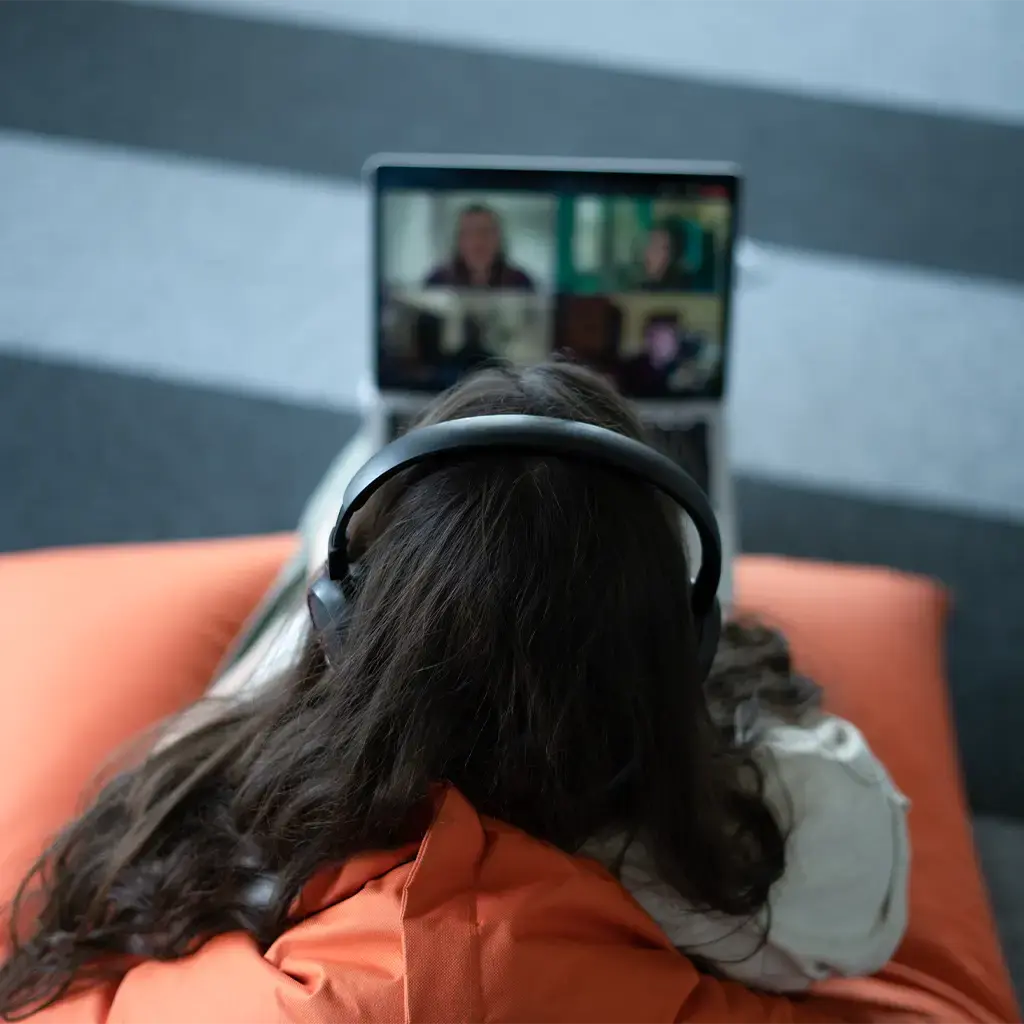Person wearing headphones joining a video call on a laptop while seated on an orange cushion.
