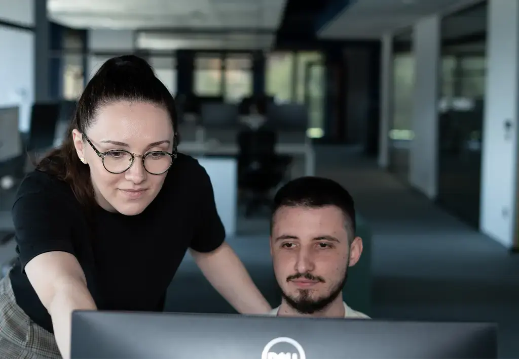 Two colleagues collaborating on a project at a computer in a modern office setting.