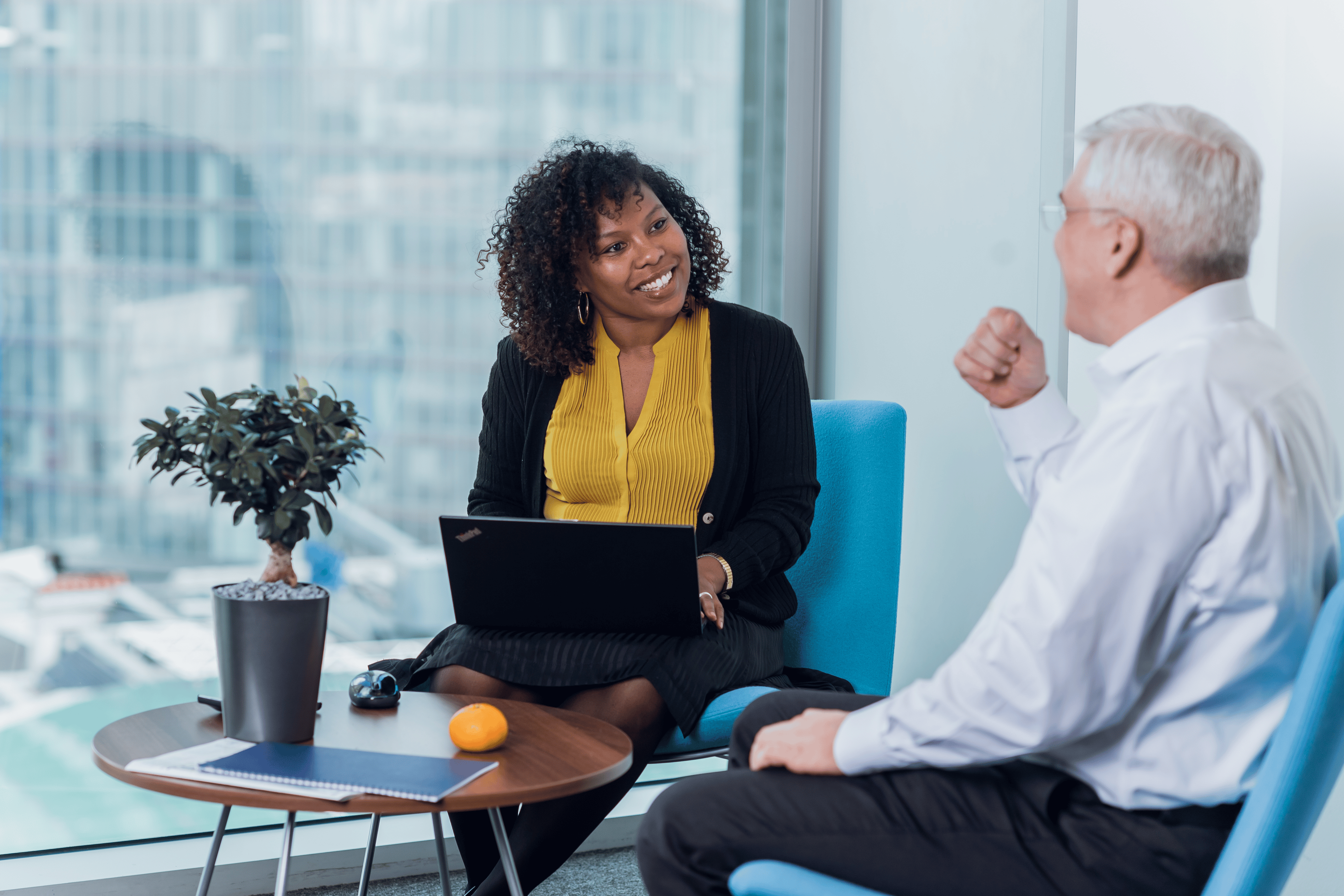 two people sitting by a window in a work environment talking with a positive atmosphere as they both smile