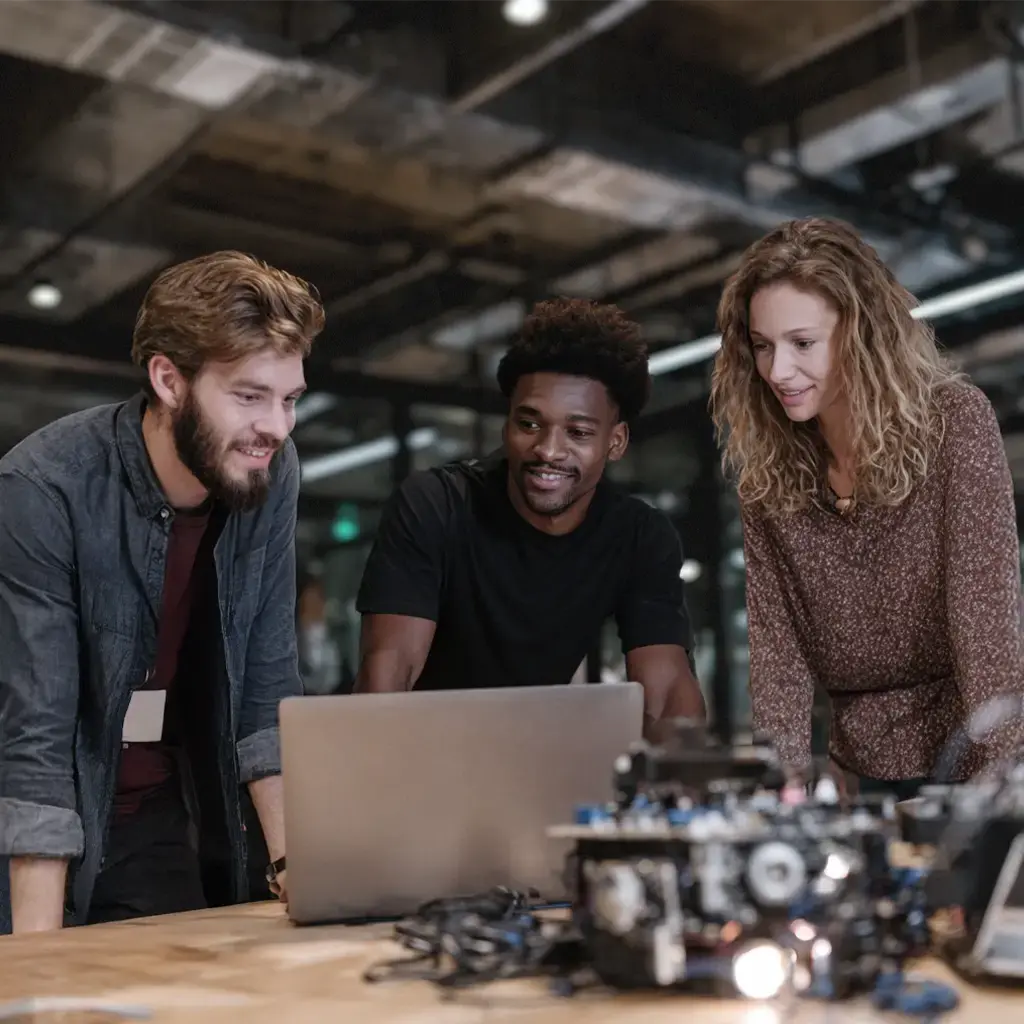Team collaborating on AI development using laptop and hardware components in modern workspace.