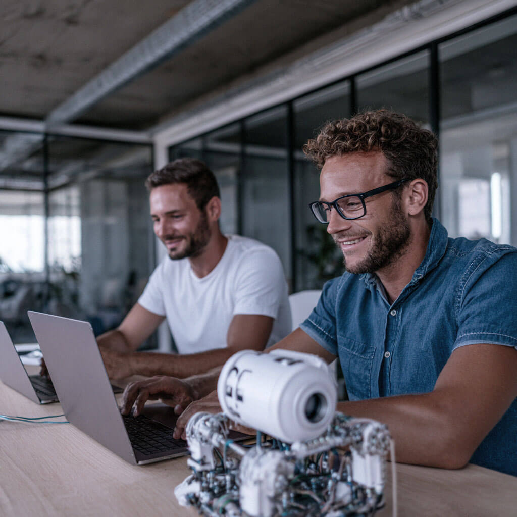 Developers working on laptops with a robotic device, highlighting innovation in AI and automation
