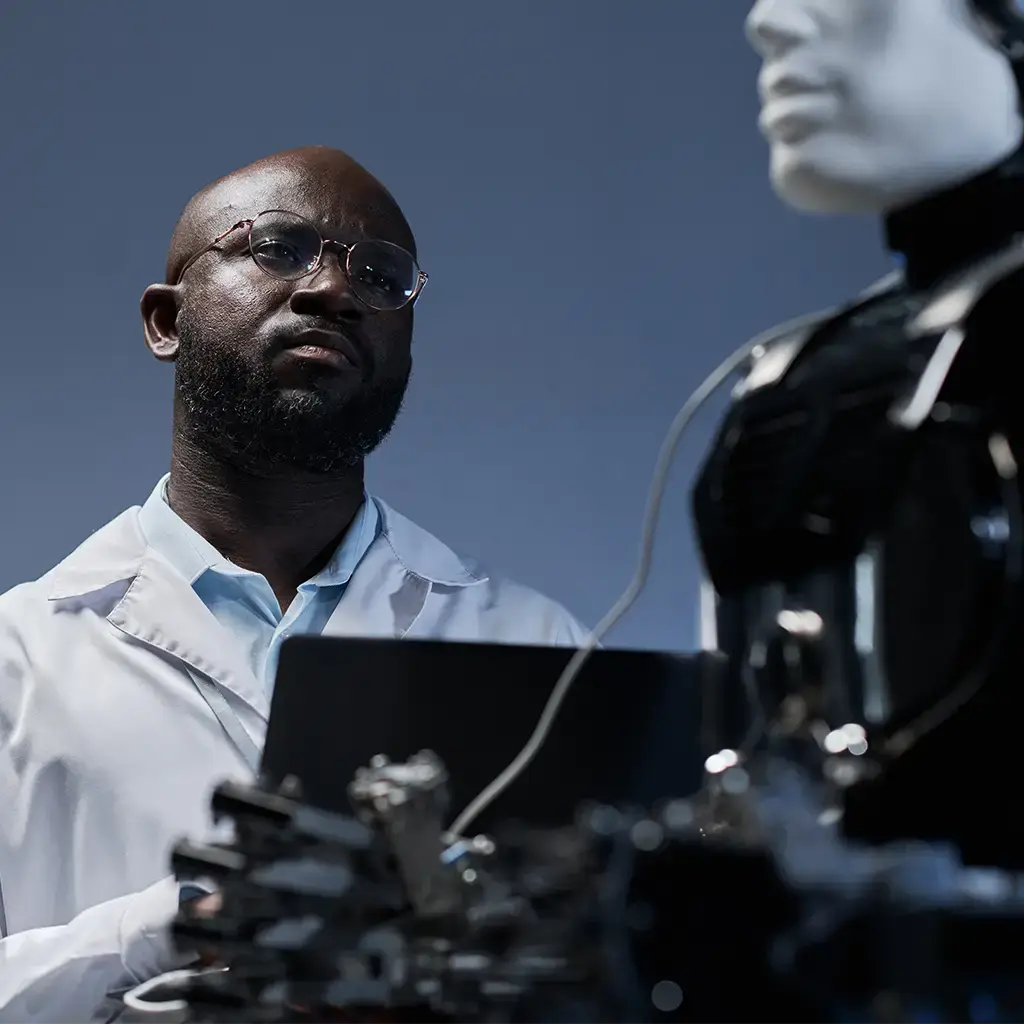 Engineer analyzing humanoid robot with a laptop in a robotics lab.