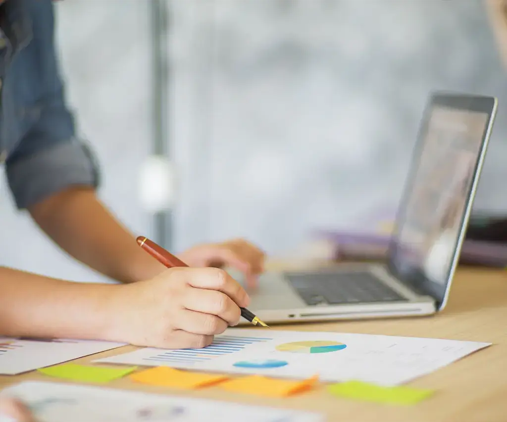 Person analyzing charts and graphs on paper while working on a laptop at a desk.