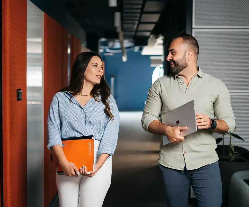 Two professionals walking through a modern office hallway, engaged in conversation.