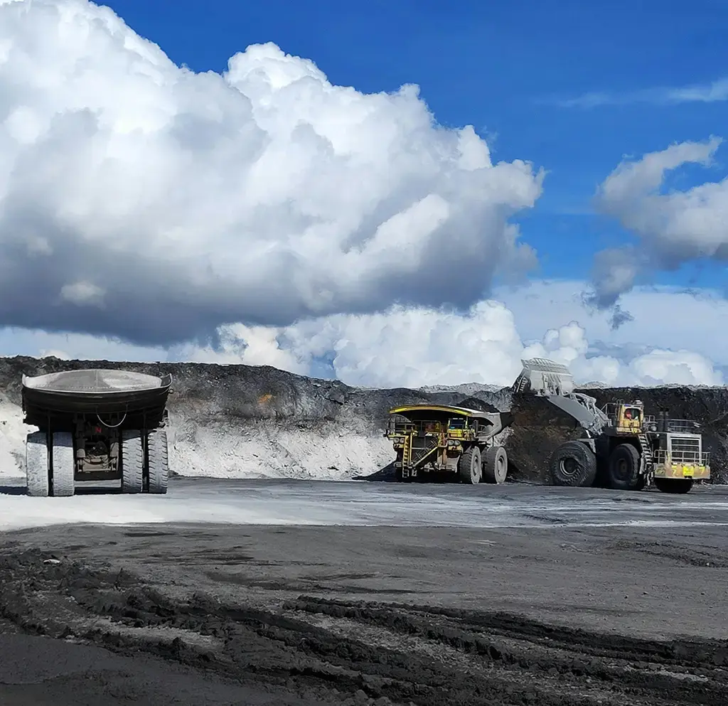 Heavy-duty mining trucks and loader operating at an open-pit mine under a bright blue sky with clouds.