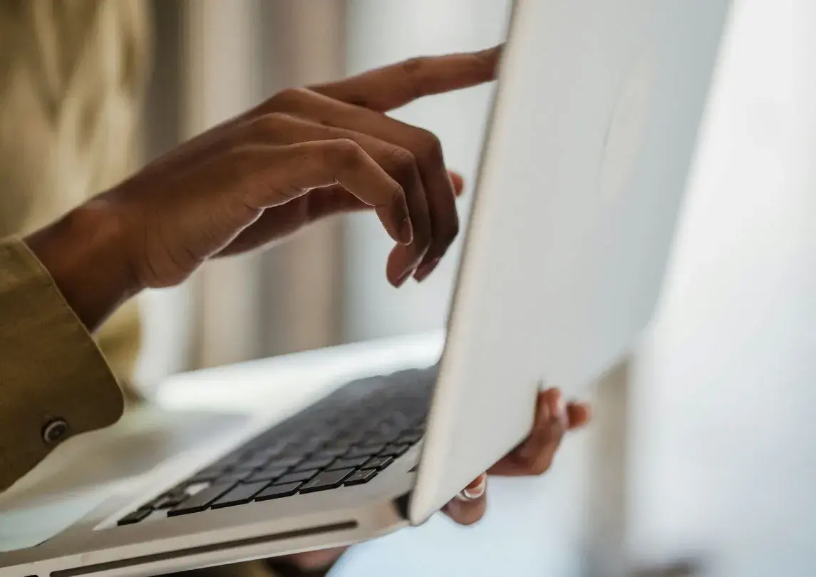 A person holding a laptop in one hand and point at the screen with the other one,