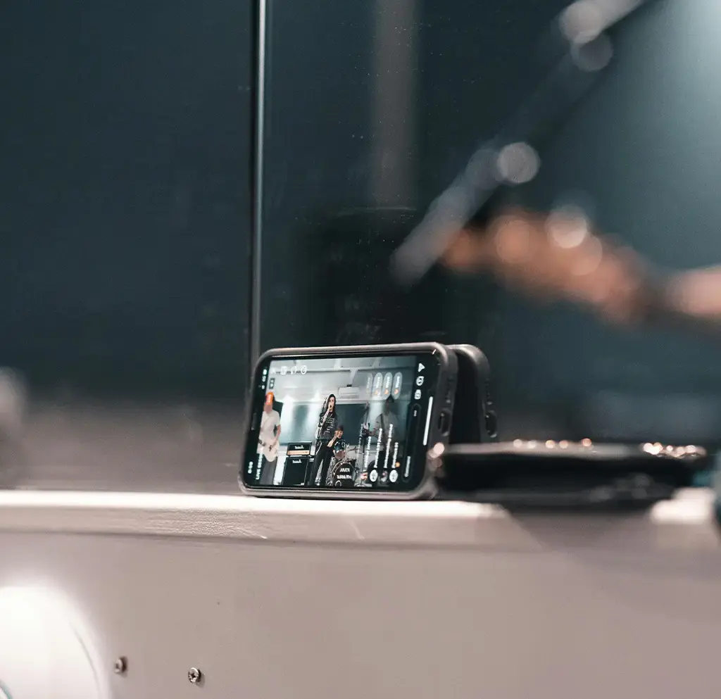 Smartphone streaming a live music performance, placed on a ledge in a dimly lit venue.