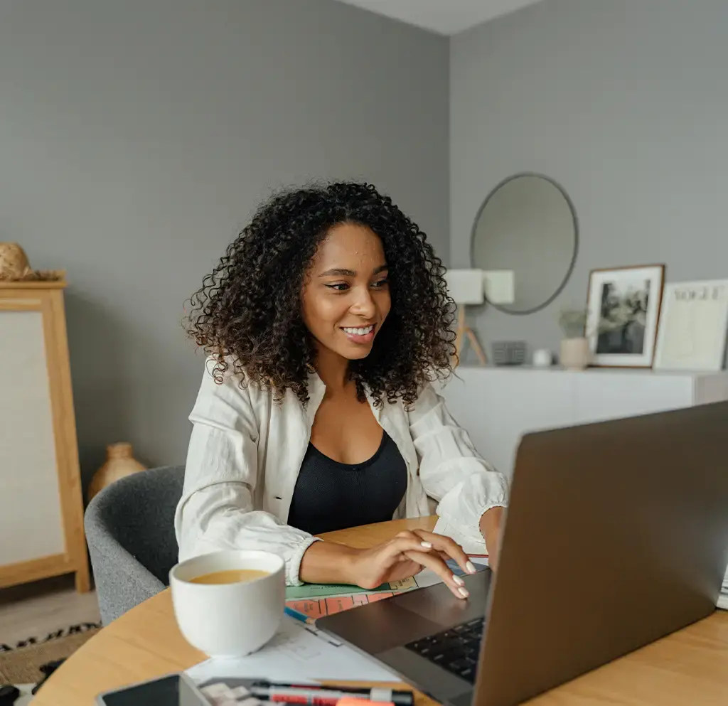 Professional working remotely at a desk with a laptop, documents, and a coffee mug.