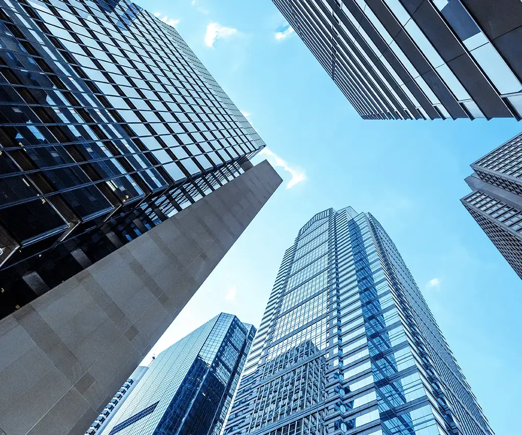 Upward view of modern glass skyscrapers against a clear blue sky in a business district.