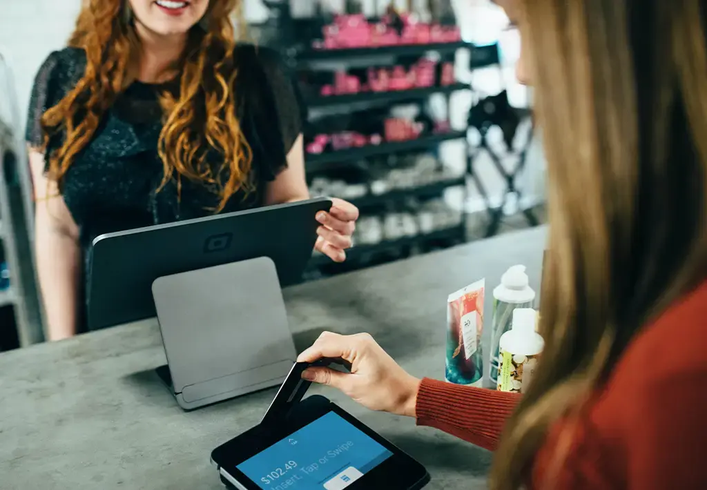 Customer tapping a card on a digital payment terminal at a retail counter using modern POS technology.