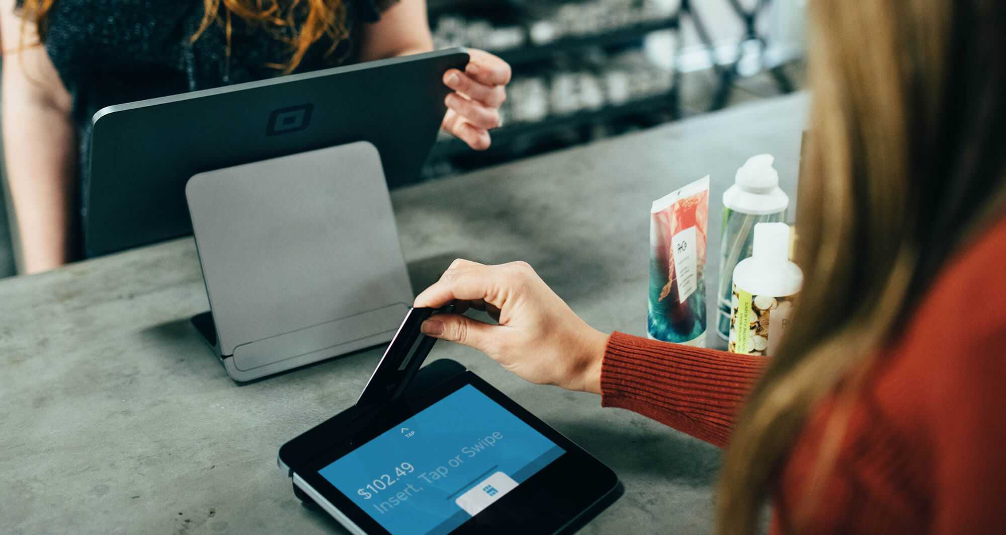Customer tapping a card on a digital payment terminal at a retail counter using modern POS technology.