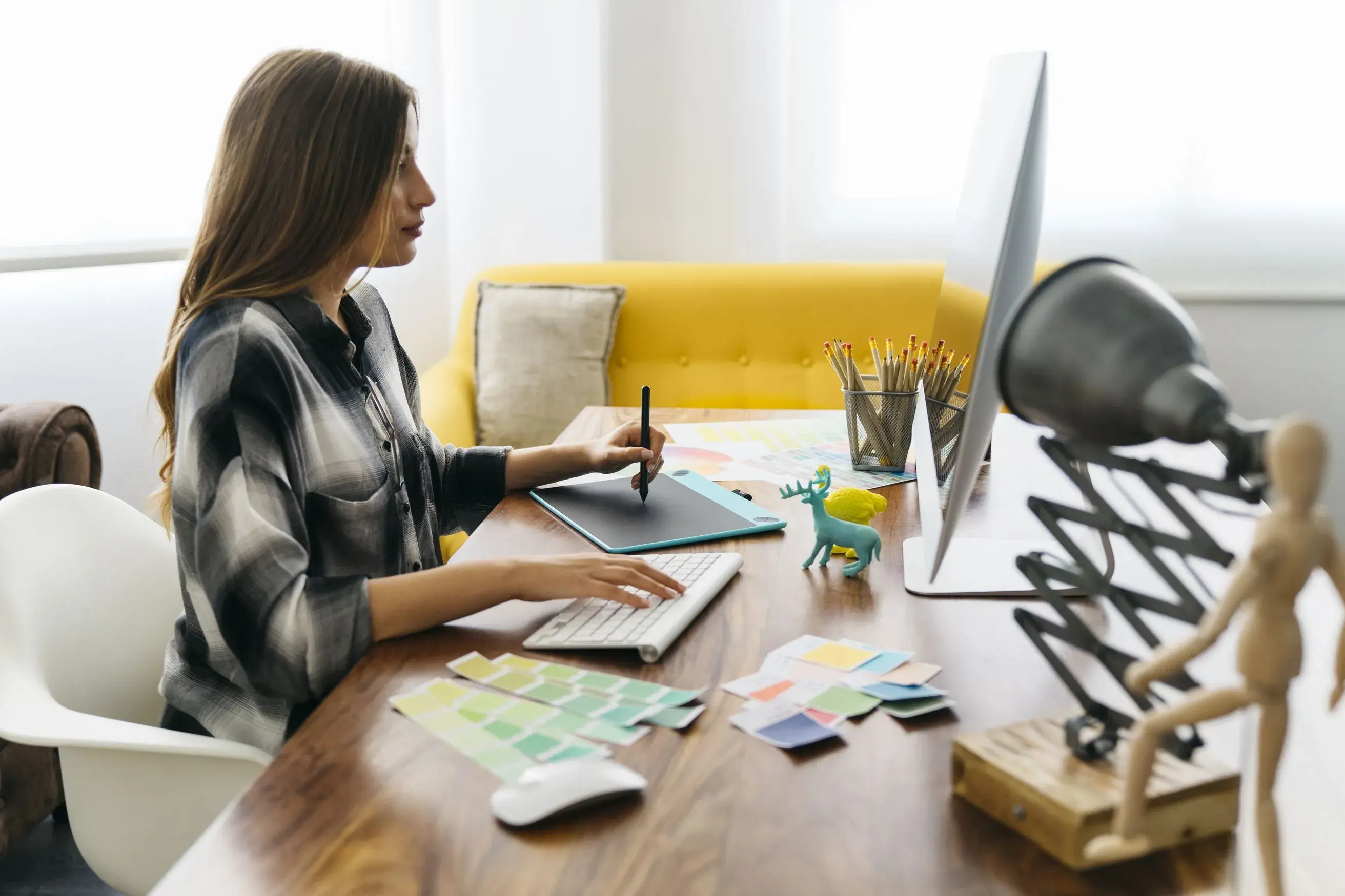 A woman seated at a desk with a computer and a yellow chair, aiding a creative software services provider in becoming cloud-agnostic.