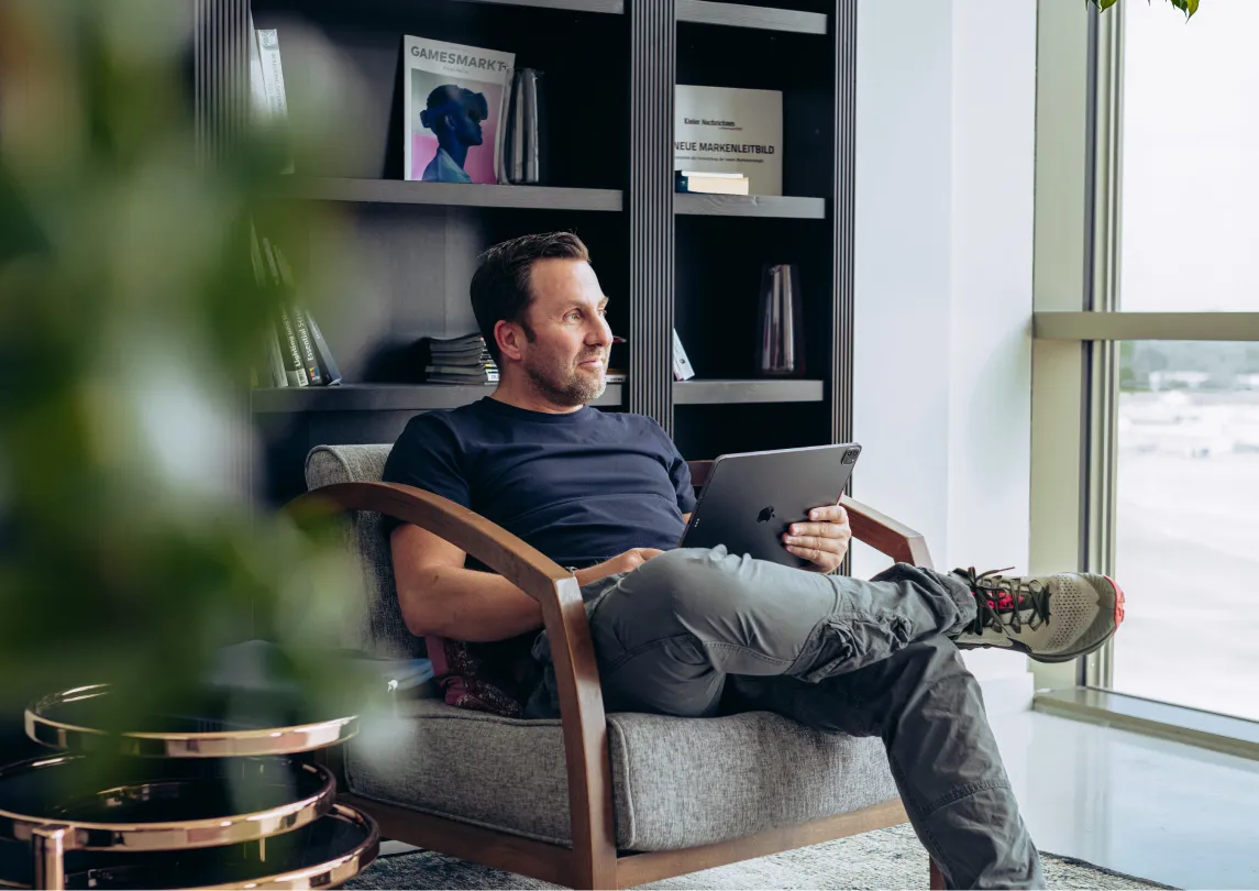 A man sitting on a chair holding a laptop looking out the window