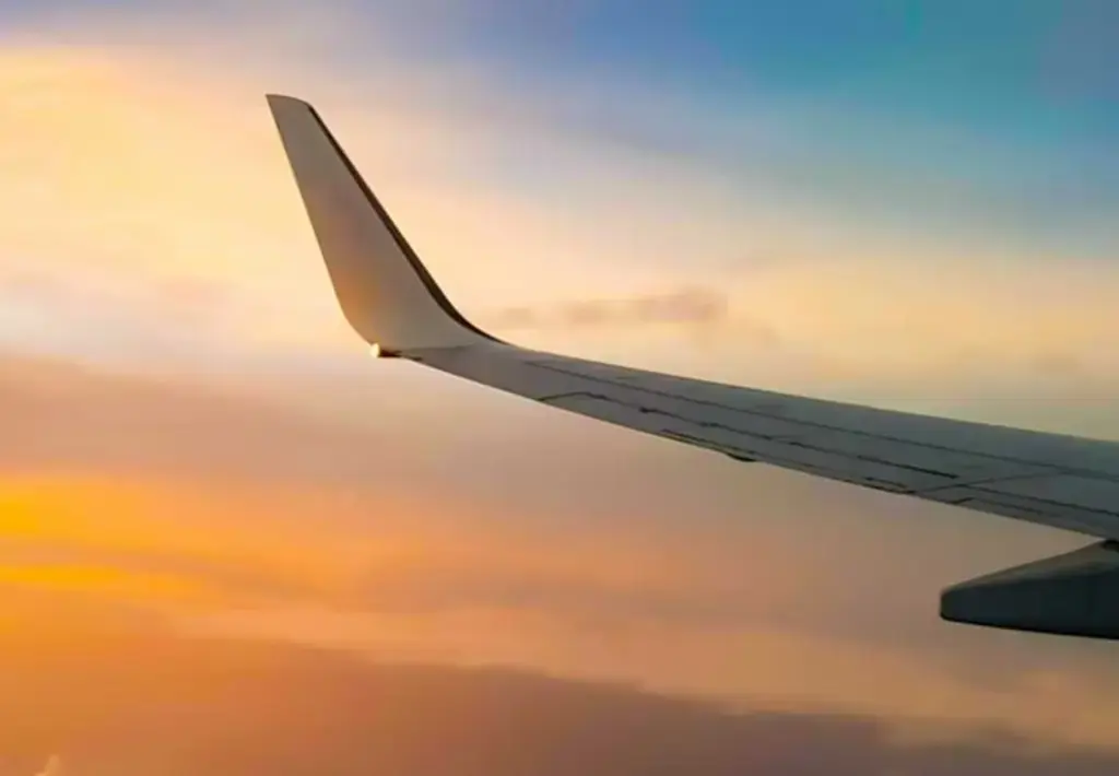 Airplane wing above the clouds during a colorful sunset, symbolizing global connectivity and travel technology.