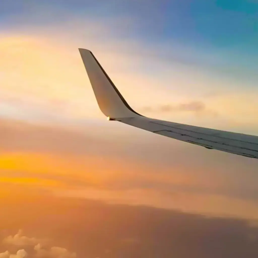 Airplane wing above the clouds during a colorful sunset, symbolizing global connectivity and travel technology.