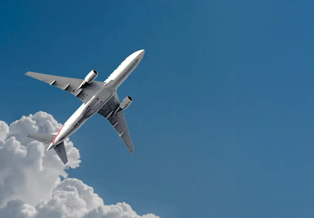Commercial airplane ascending above clouds against clear blue sky, representing travel technology.