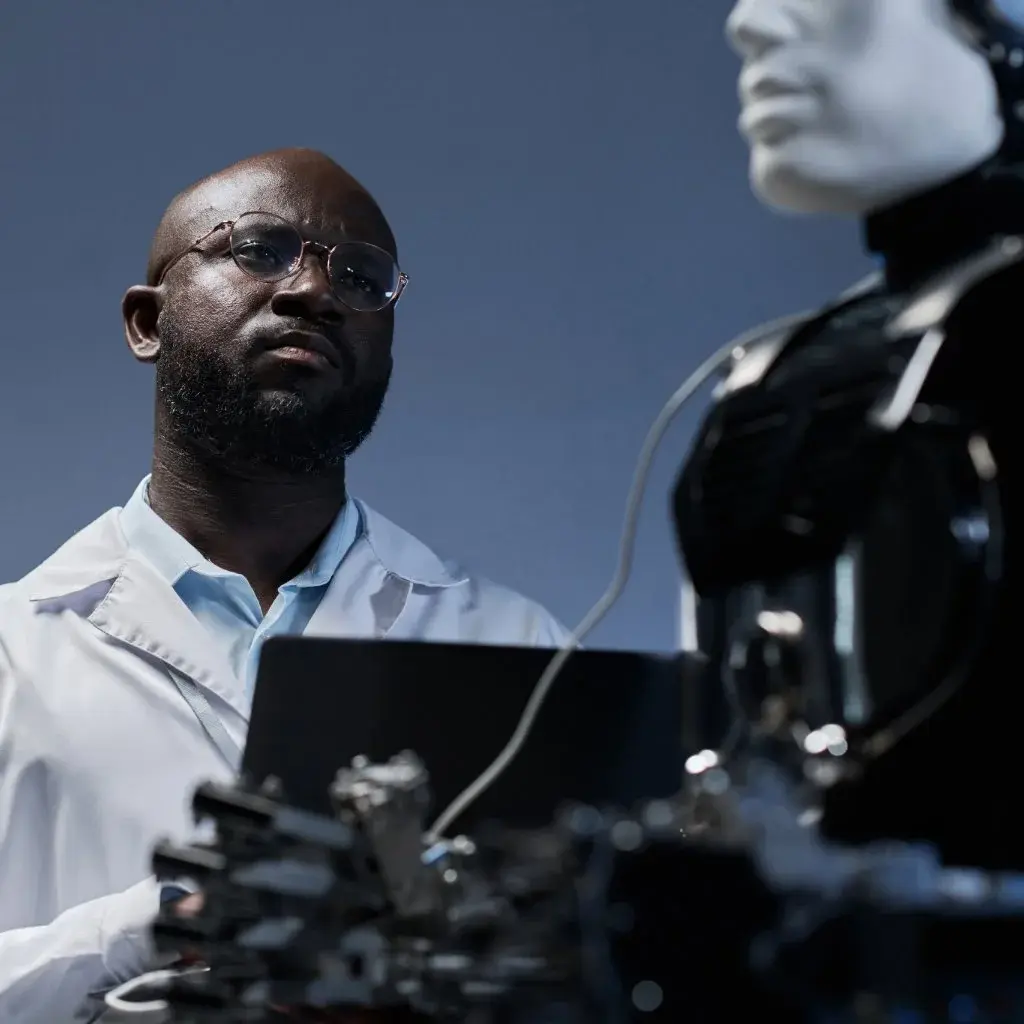 Engineer in lab coat analyzing humanoid robot connected to a laptop.