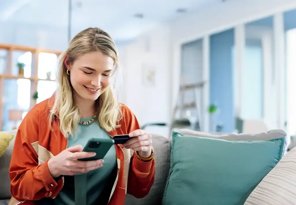 Smiling customer making a mobile payment from home using a smartphone and credit card.