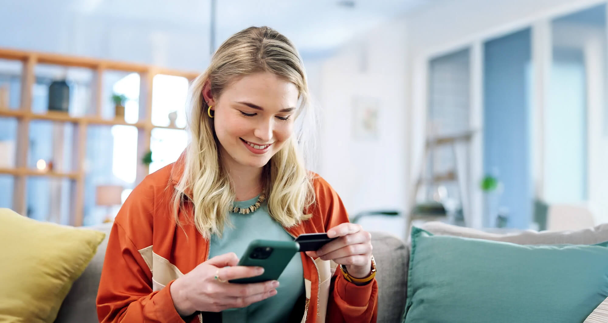Smiling customer making a mobile payment from home using a smartphone and credit card.