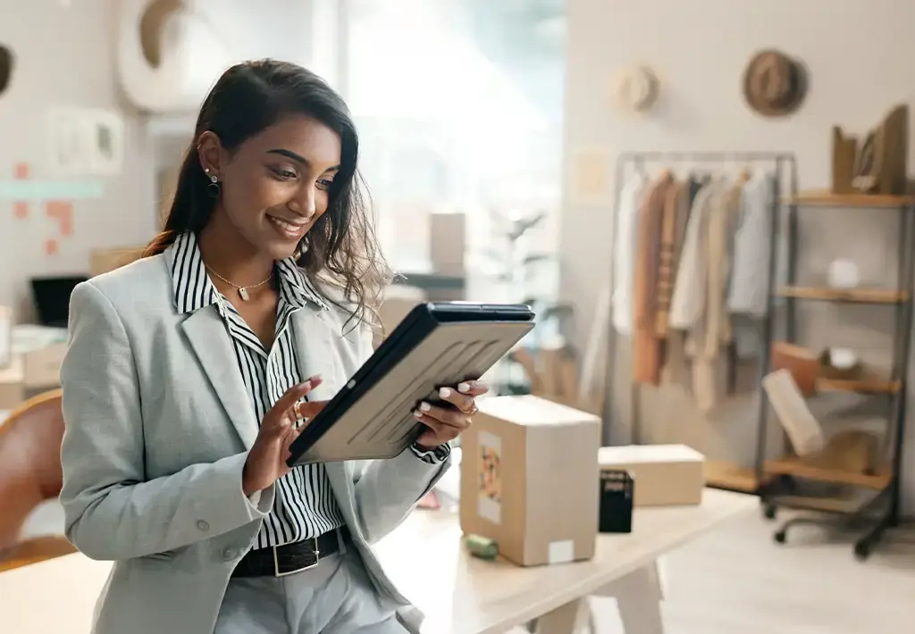 Retail business owner using a tablet to streamline order management in a product-packed workspace.