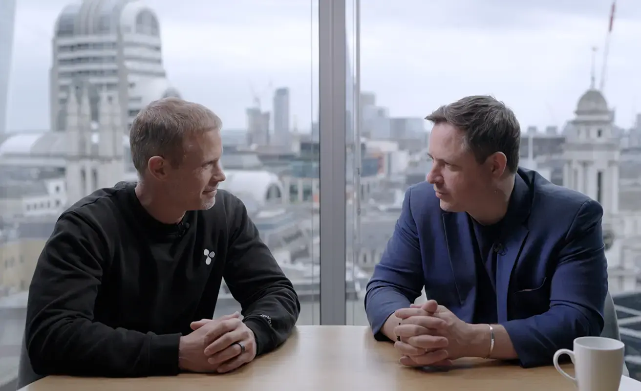 Two business professionals in conversation at a London office with a city skyline view.