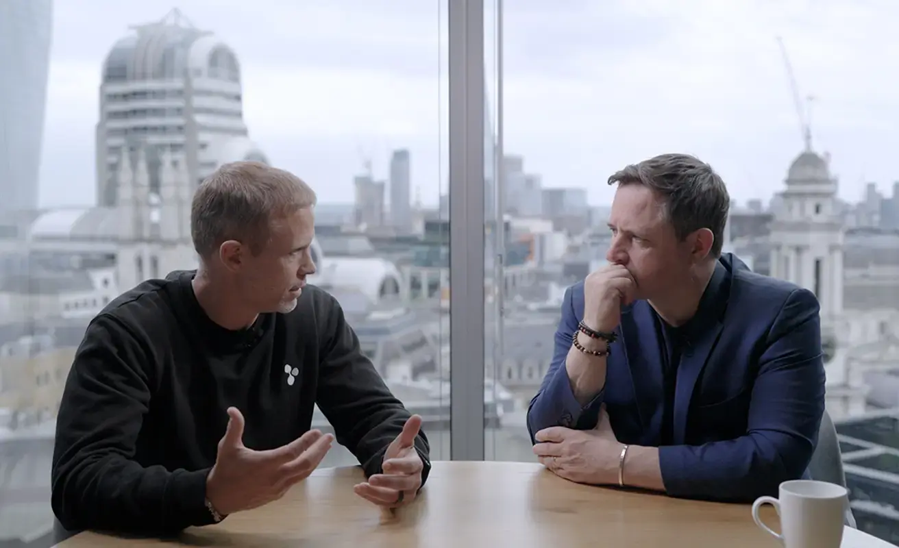 Two business professionals in conversation at a London office with a city skyline view.