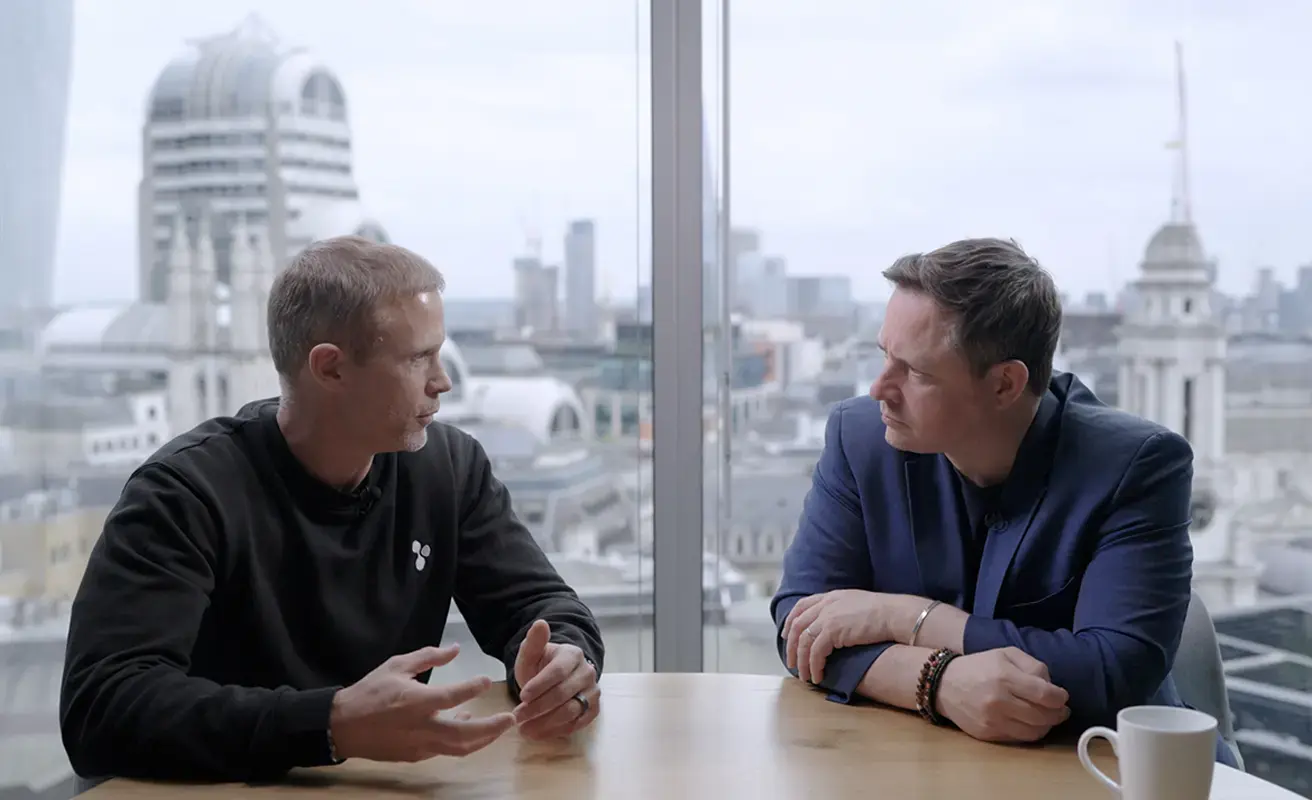 Two business professionals in conversation at a London office with a city skyline view.