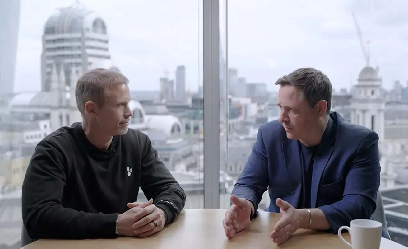 Two business professionals in conversation at a London office with a city skyline view.