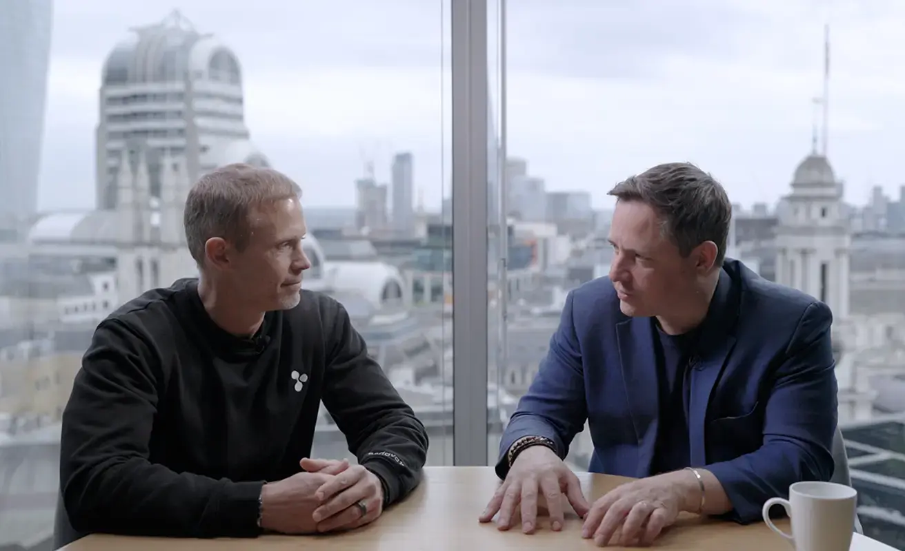 Two business professionals in conversation at a London office with a city skyline view.