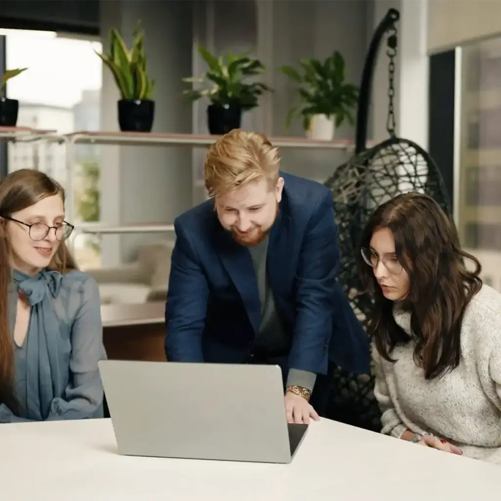 Three professionals collaborating around a laptop in a modern office setting.
