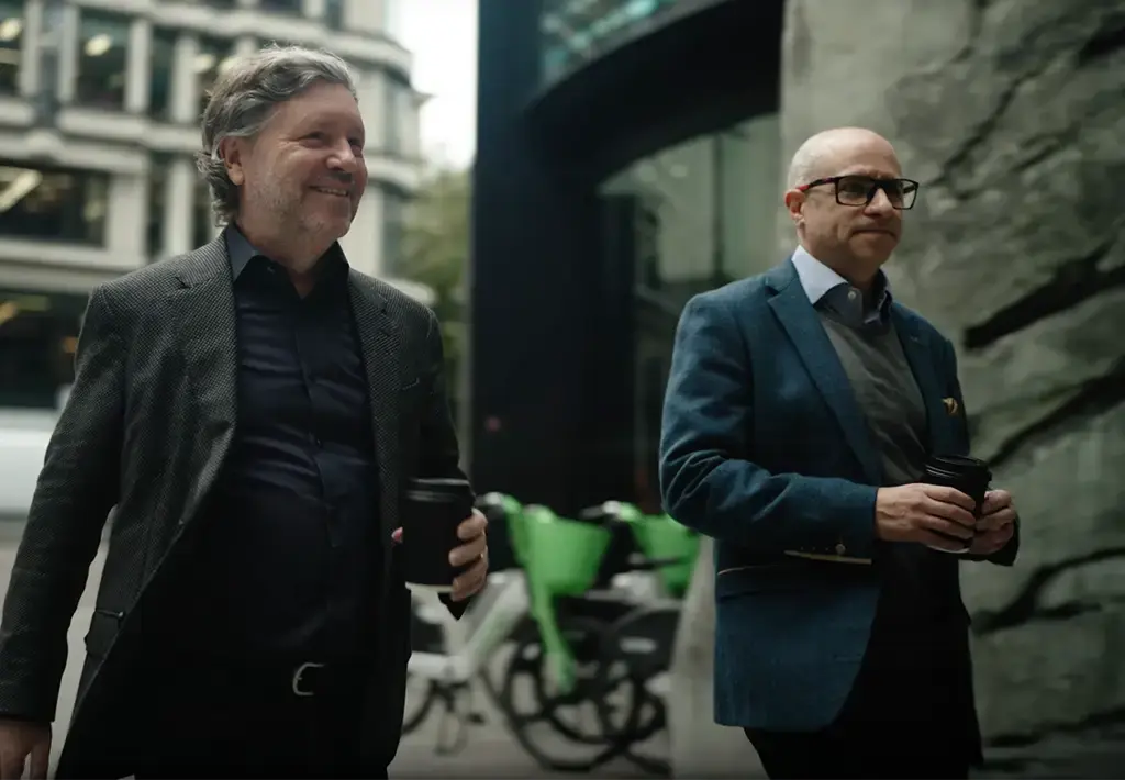 Endava CEO John Cotterell walking through a city with a colleague, both holding coffee cups and engaged in conversation