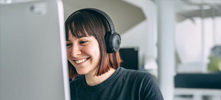 Smiling employee wearing headphones and working at a computer, reflecting focus and job satisfaction.