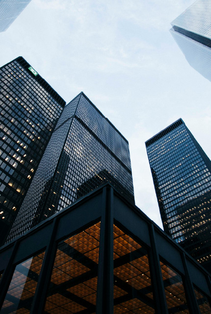 Low-angle view of tall glass office buildings against a cloudy sky.