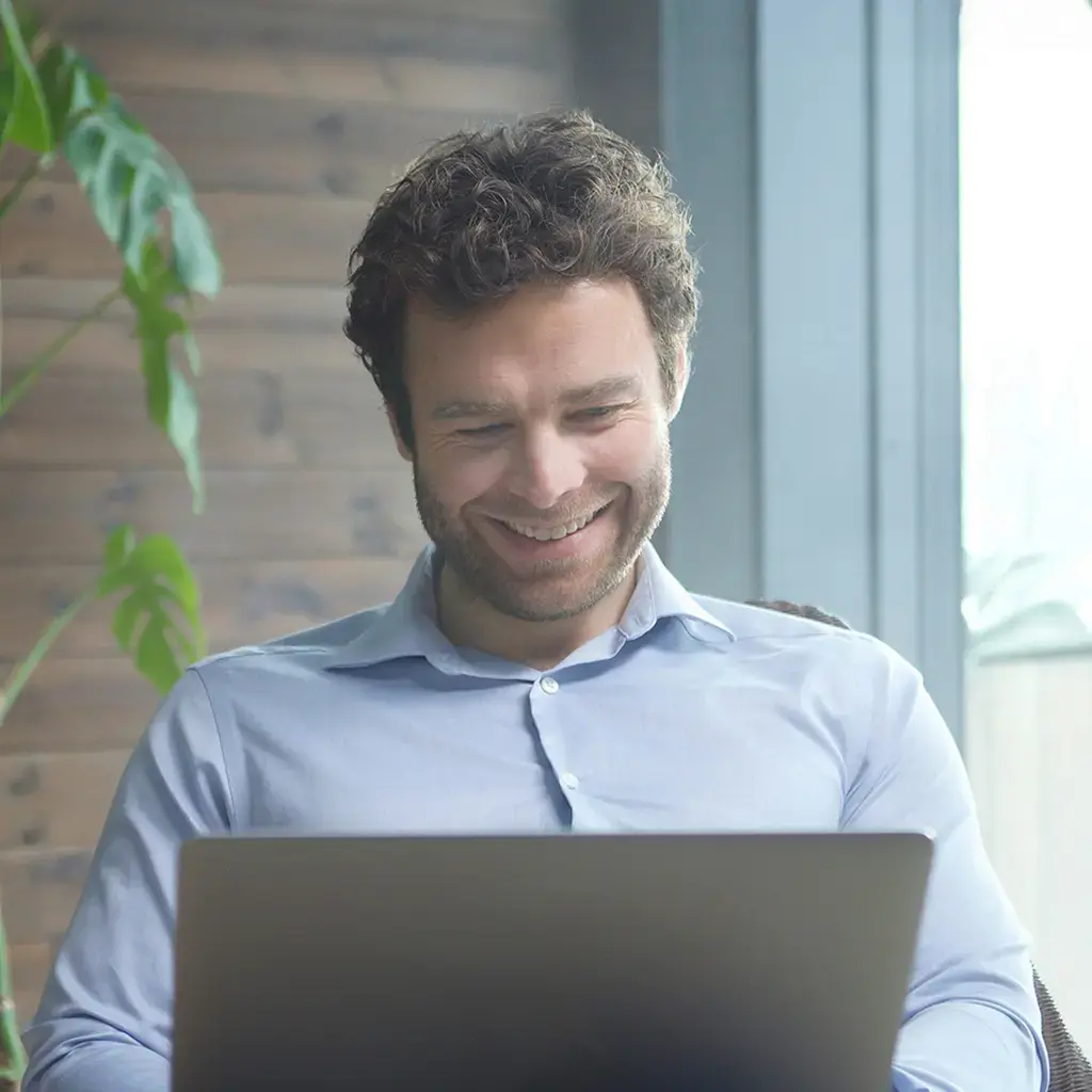Professional working remotely on a laptop in a bright, modern environment with greenery